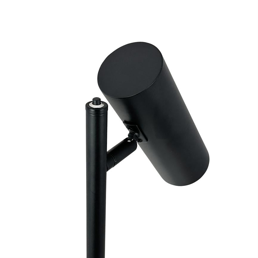 Sort cylinderformet spotlampe monteret på en lodret metalstang, svagt vinklet nedad, med et lille hængsel ved fatningen; enkel, neutral hvid baggrund.