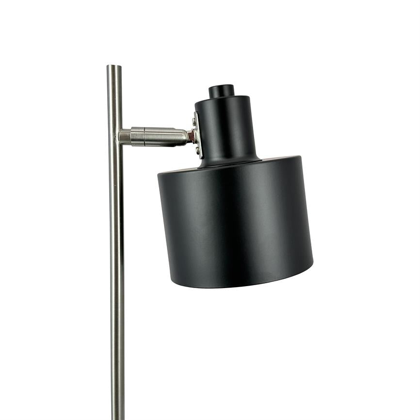 Standerlampe med sort cylindrisk skærm; skærmen er vippet fremad og monteret på en slank, børstet sølvfarvet metalstang, placeret mod en ren hvid baggrund.