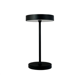 Sort bordlampe står oprejst med flad, rund skærm, tynd midterstang og cirkulær fod foran en ensartet hvid baggrund.