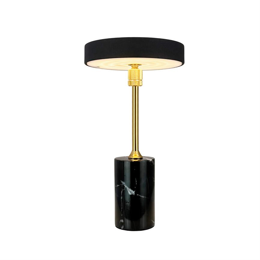 Bordlampe med sort rund skærm, gylden stang og cylindrisk sort marmorfod; lampen lyser blødt nedad og står isoleret mod en hvid baggrund.