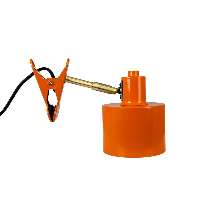 En orange klemme med sort ledning er fastgjort via et guldfarvet ledled til en orange cylindrisk lampefod på ensartet hvid baggrund.
