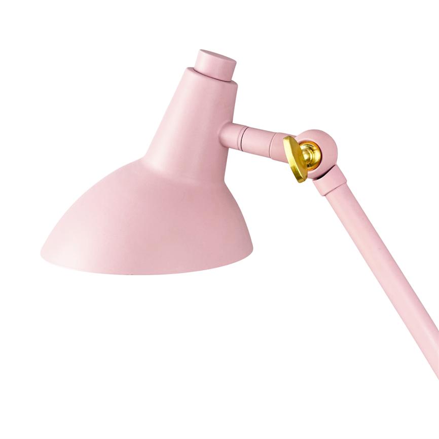 En lyserød justerbar skrivebordslampe vipper sin halvkugleformede skærm nedad via en leddelt arm med en guldfarvet skrue, placeret mod en neutral hvid baggrund.