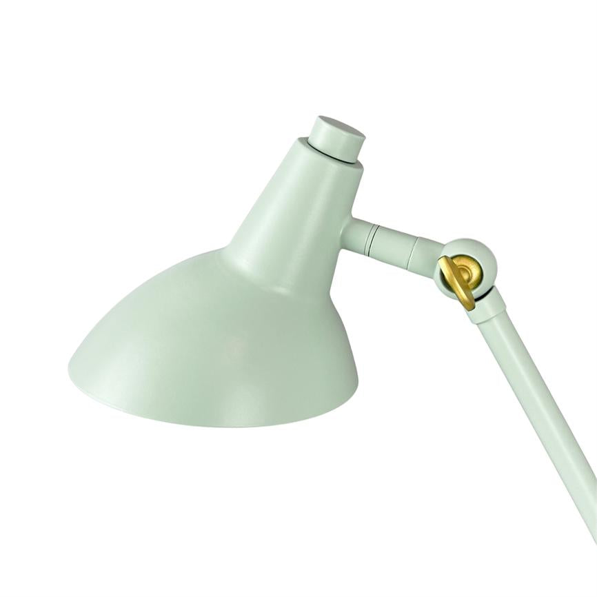 Bordlampe i mintgrøn, skærm vinklet nedad; justerbart led synligt med en messingfarvet detalje, mod ren hvid baggrund.