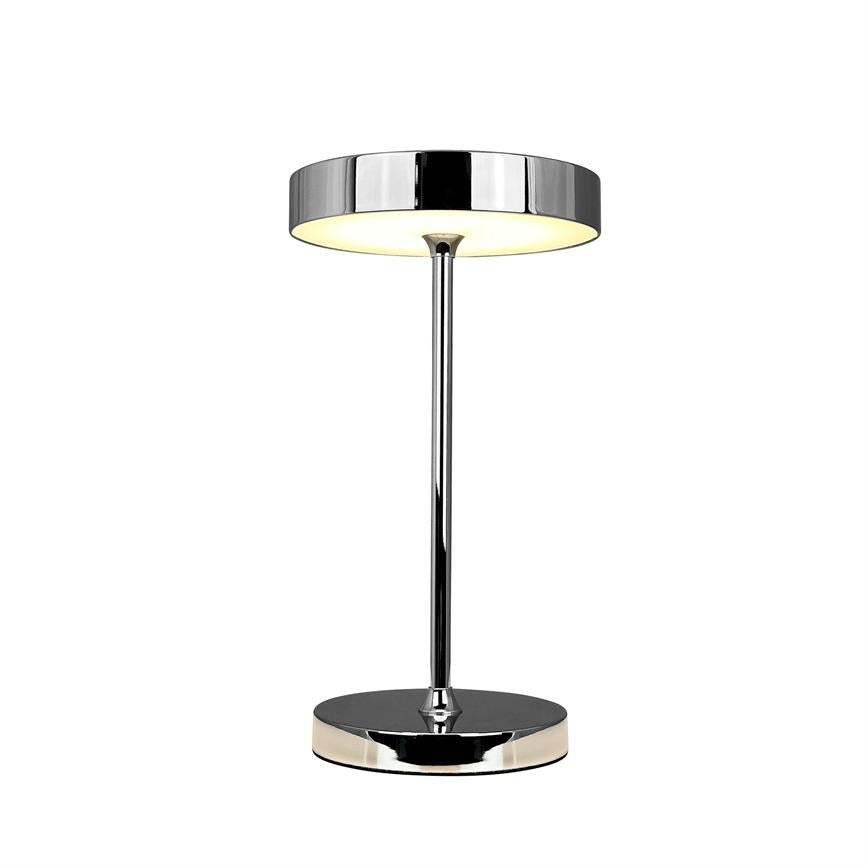 Bordlampe med rund kromskærm lyser blødt nedad; slank kromstang forbinder skærm og rund fod, alt stående mod en neutral hvid baggrund.
