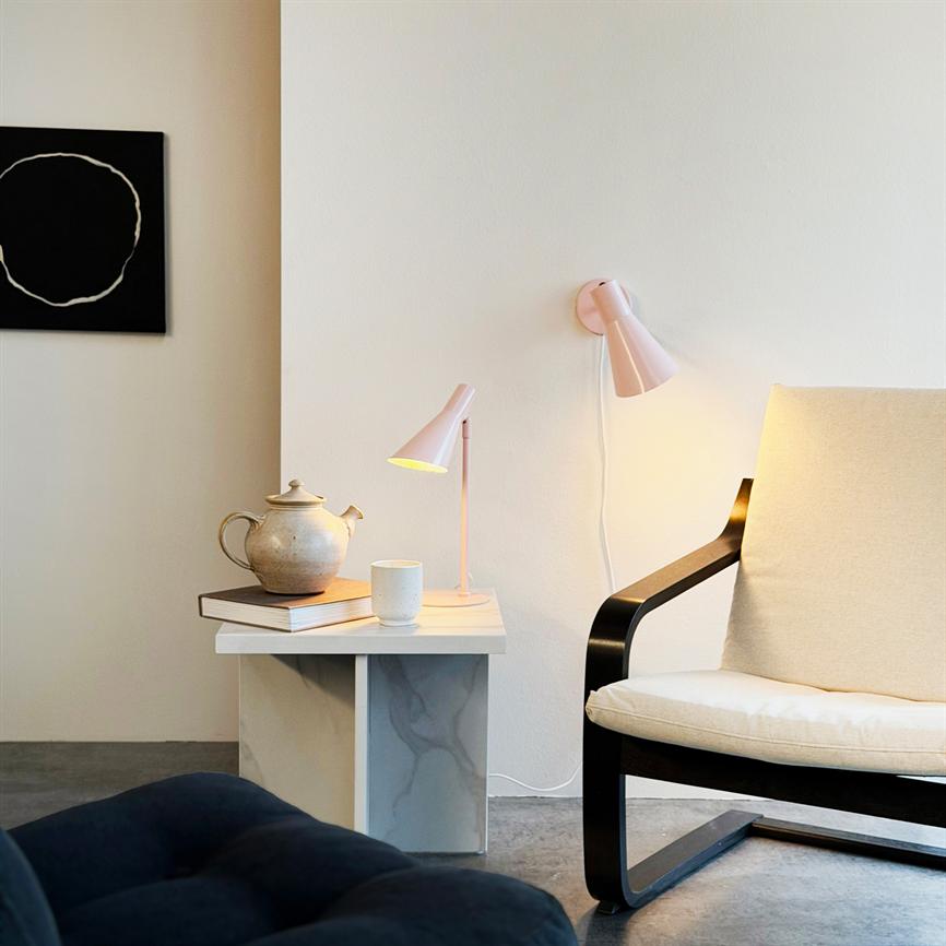 Bordlampe og væglampe kaster varmt lys over en tekande og kop, der står på bøger på et lille marmorbord. Ved siden af en lys lænestol med sort arm.
