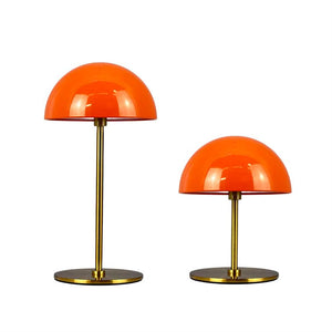 To orange, kuppelformede lamper står ved siden af hinanden — én høj, én lav — med tynde messingstænger og flade sorte baser med guldkant på ensartet hvid baggrund.